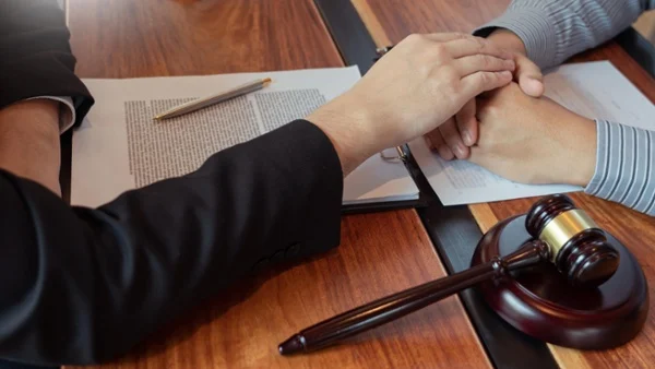 A judge's hand comforts a persons' hands that are folded over a contract